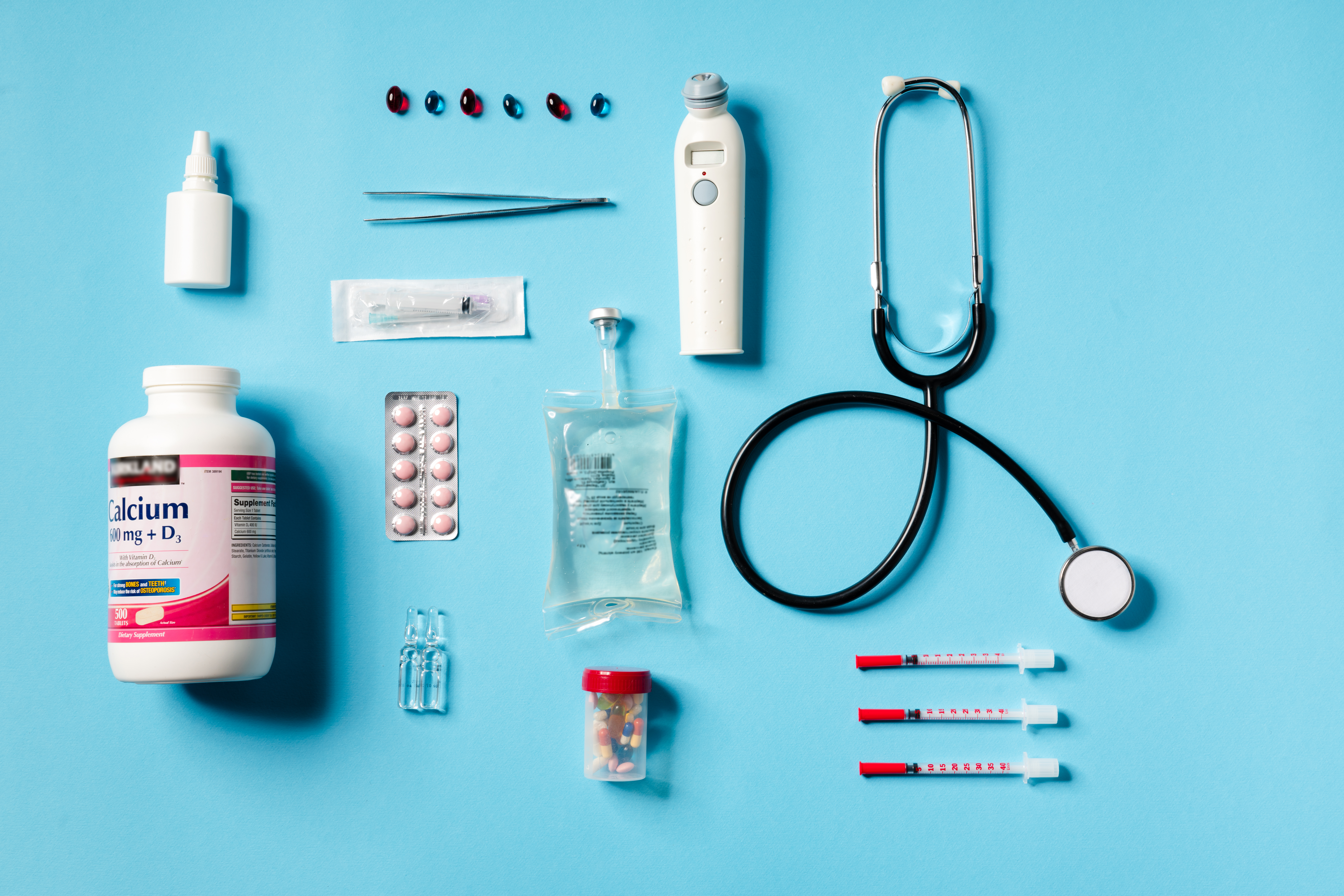 Overhead view of a medical instruments consisting of a jar of calcium, syringes, thermometer, stethoscope, tweezers lying on a blue background Overhead view of a medical instruments consisting of a jar of calcium, syringes, thermometer, stethoscope, tweezers lying on a blue background in the studio
